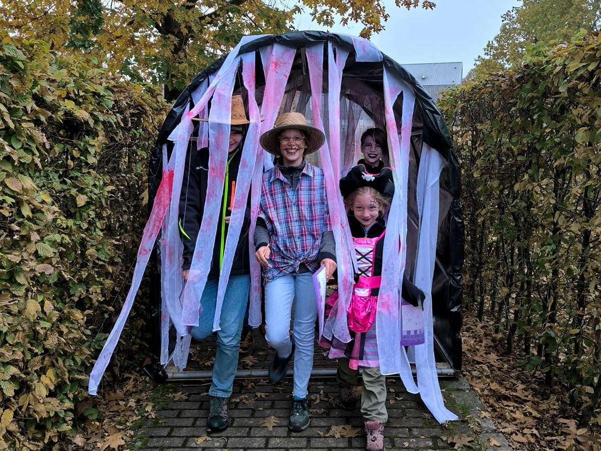 A family walking out of a tunnel hung with ghostly white streamers in a hedge maze